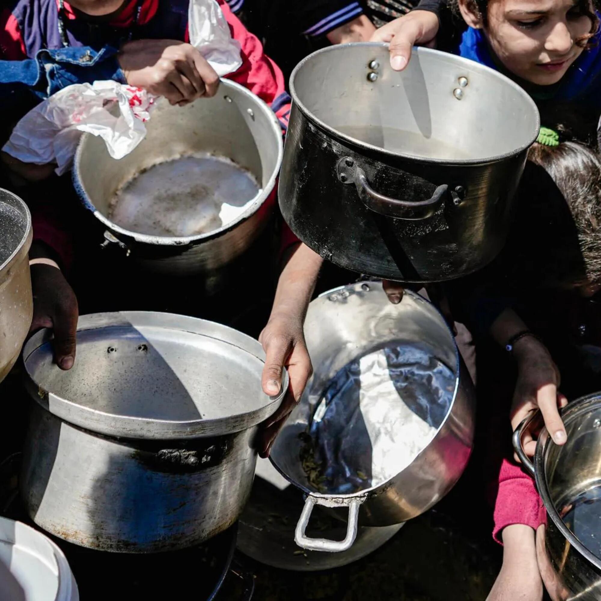 Niños y niñas sostienen sus ollas vacías en una cocina comunitaria en el norte de Gaza