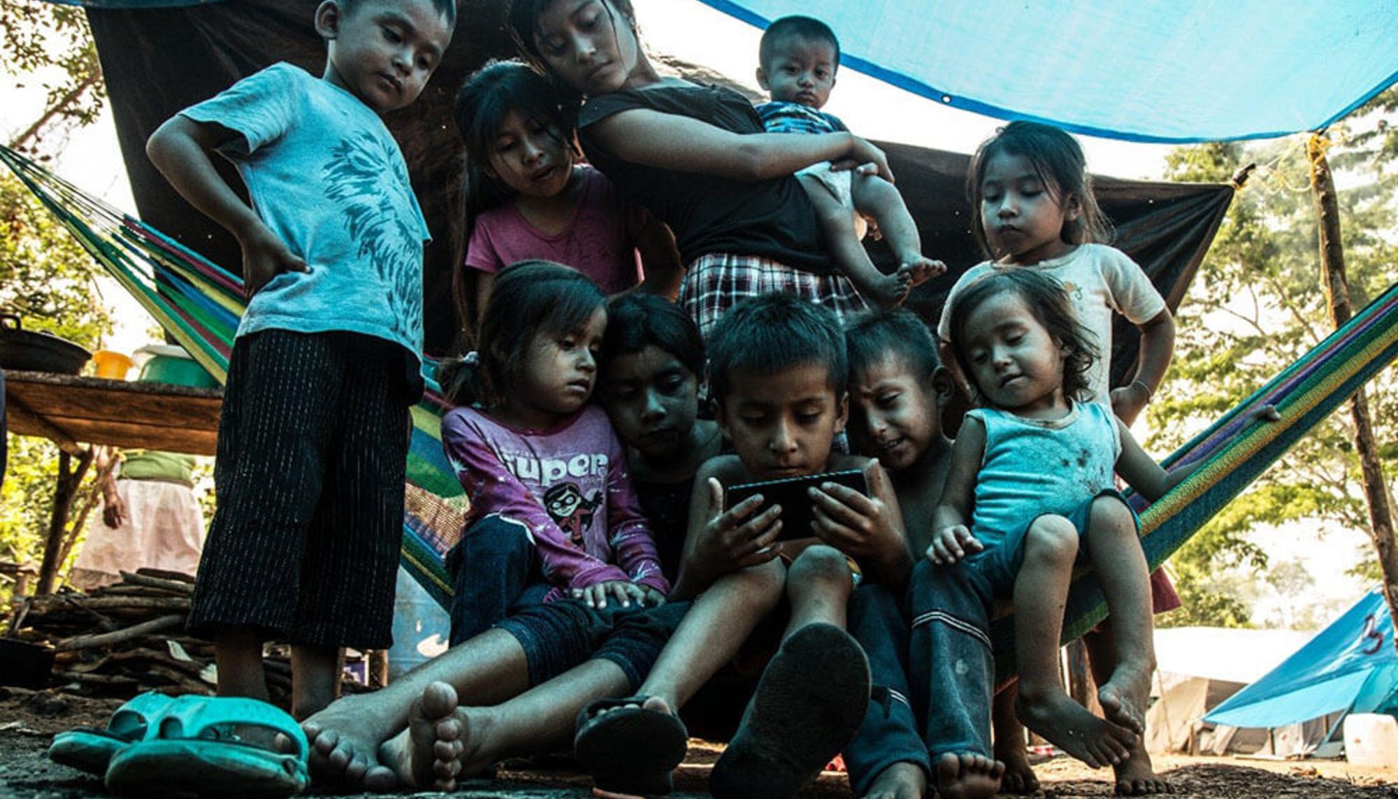 Un grupo de niños, Patojos que observan vídeos en un teléfono móvil. Aunque en la zona no hay señal, los teléfonos sirven para escuchar la radio, ver vídeos o escuchar música