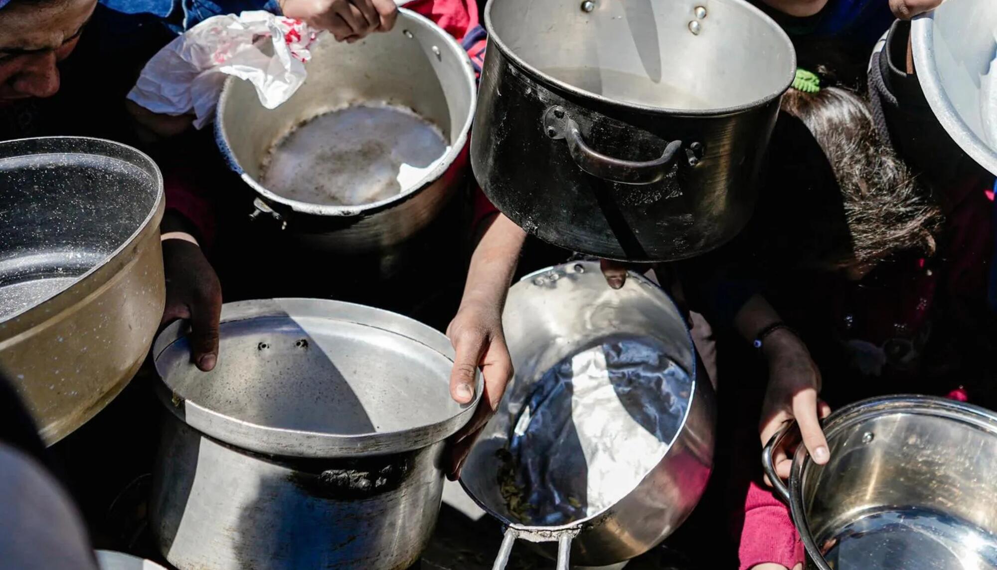 Niños y niñas sostienen sus ollas vacías en una cocina comunitaria en el norte de Gaza