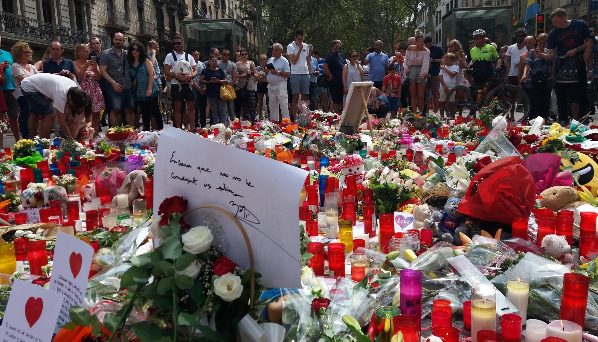 Personas observan las flores que se han puesto por la conmemorar las víctimas de los atentados de Barcelona y Cambrils, en las Ramblas 