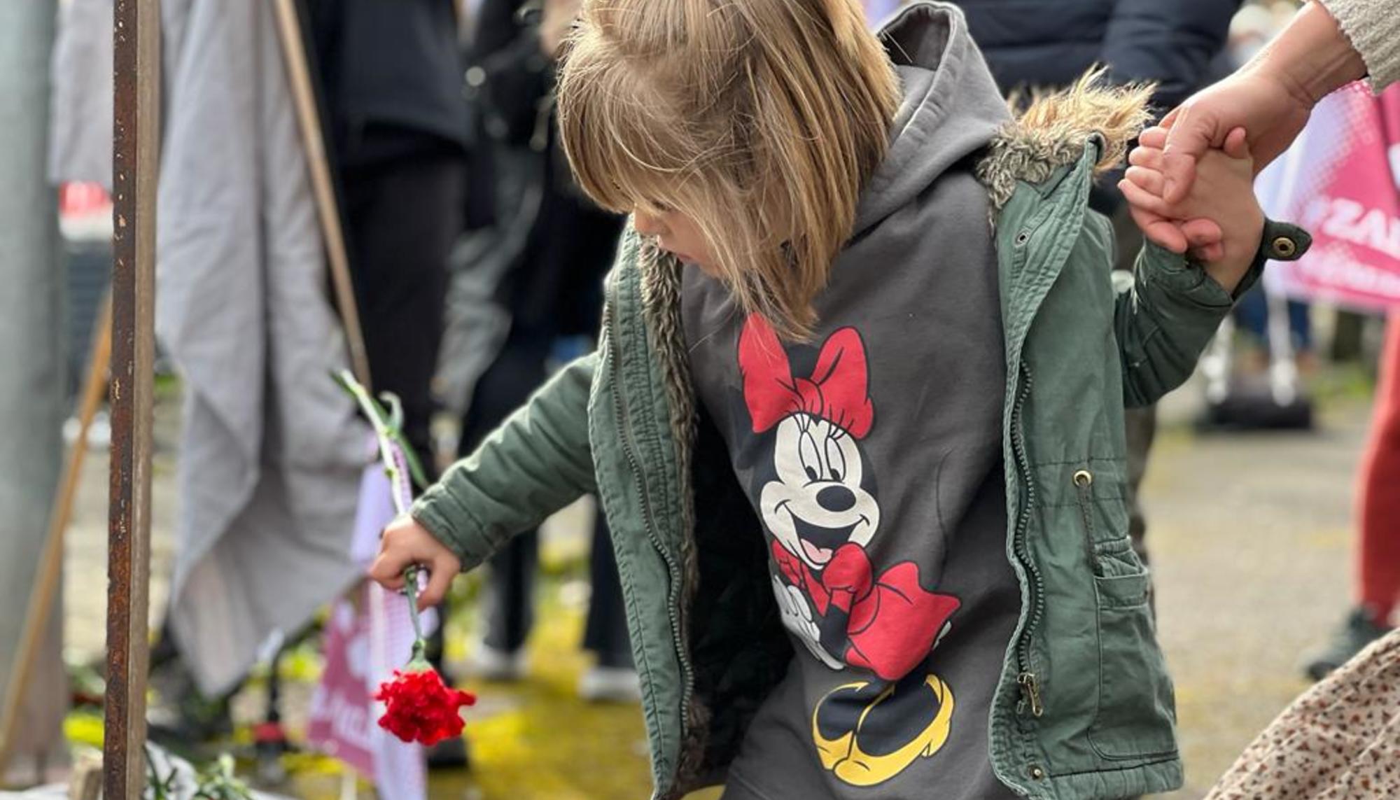Una niña coloca una rosa sobre el monumento conmemorativo de las víctimas
