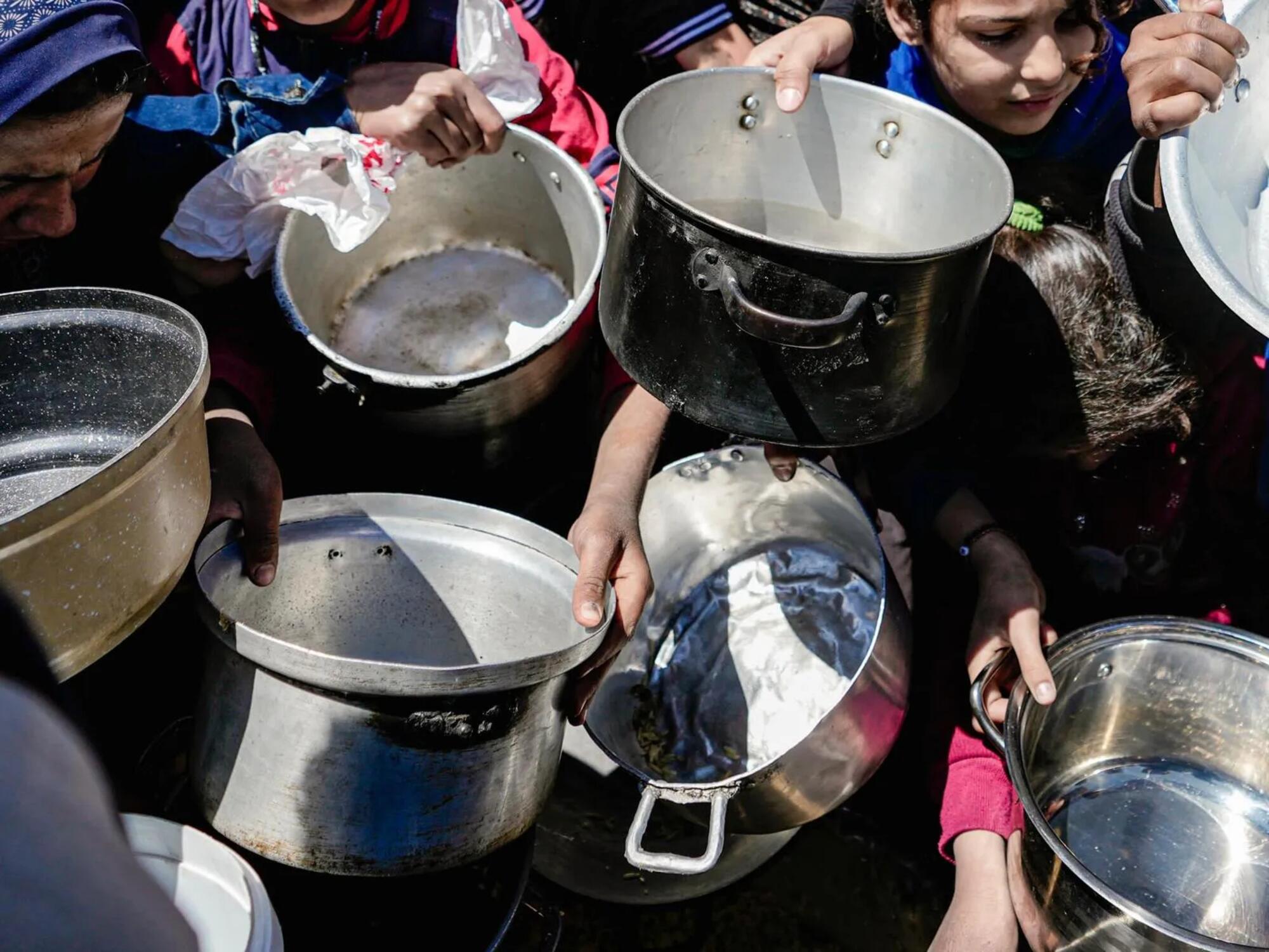 Niños y niñas sostienen sus ollas vacías en una cocina comunitaria en el norte de Gaza