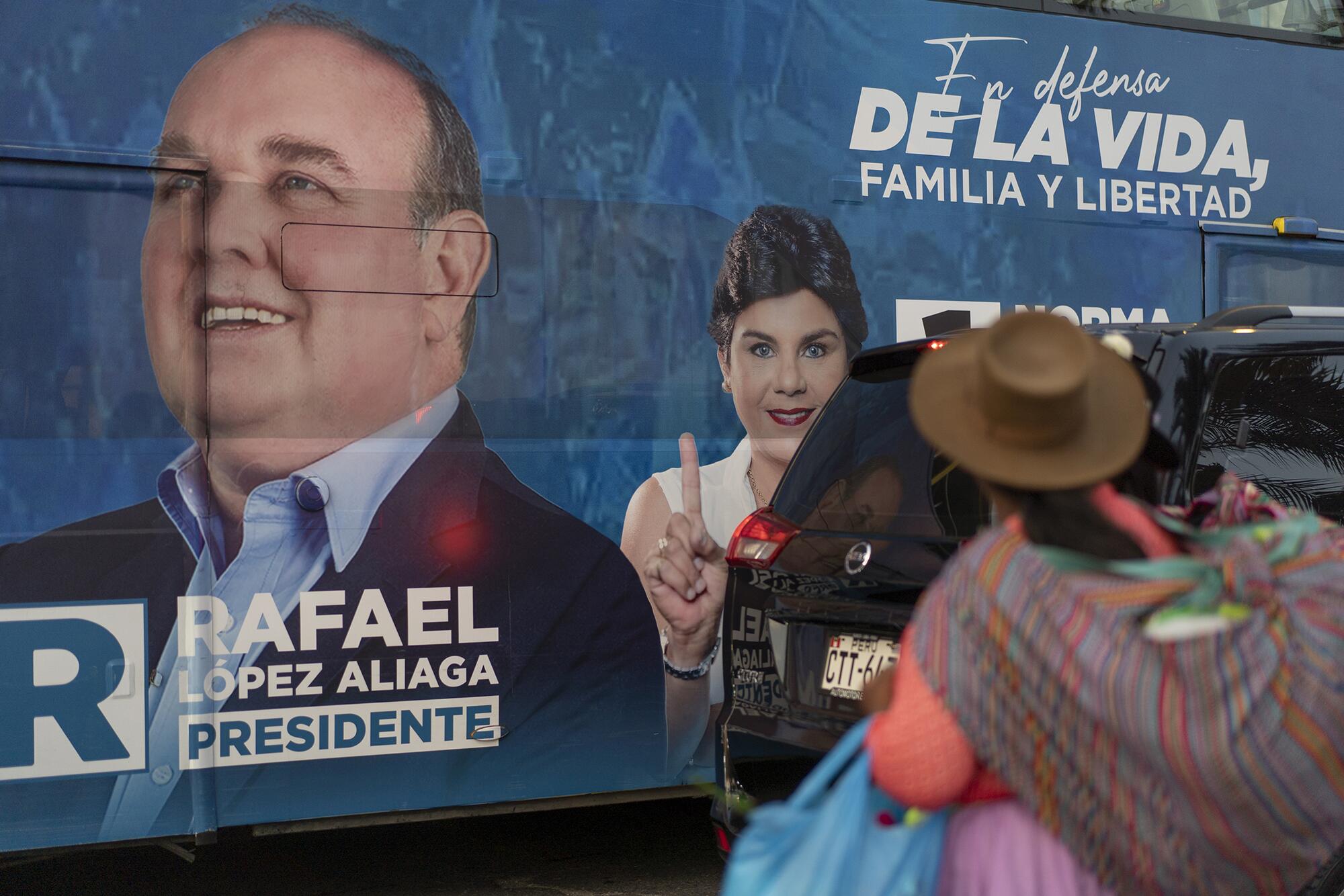 Una mujer con la característica vestimenta de altiplano peruano observa el autobús de propaganda electoral de López Aliaga.