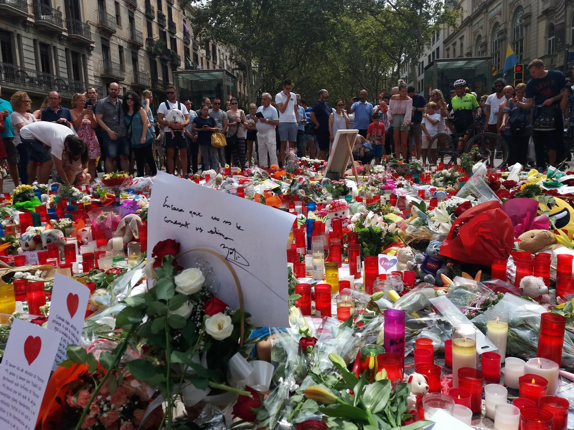 Personas observan las flores que se han puesto por la conmemorar las víctimas de los atentados de Barcelona y Cambrils, en las Ramblas 