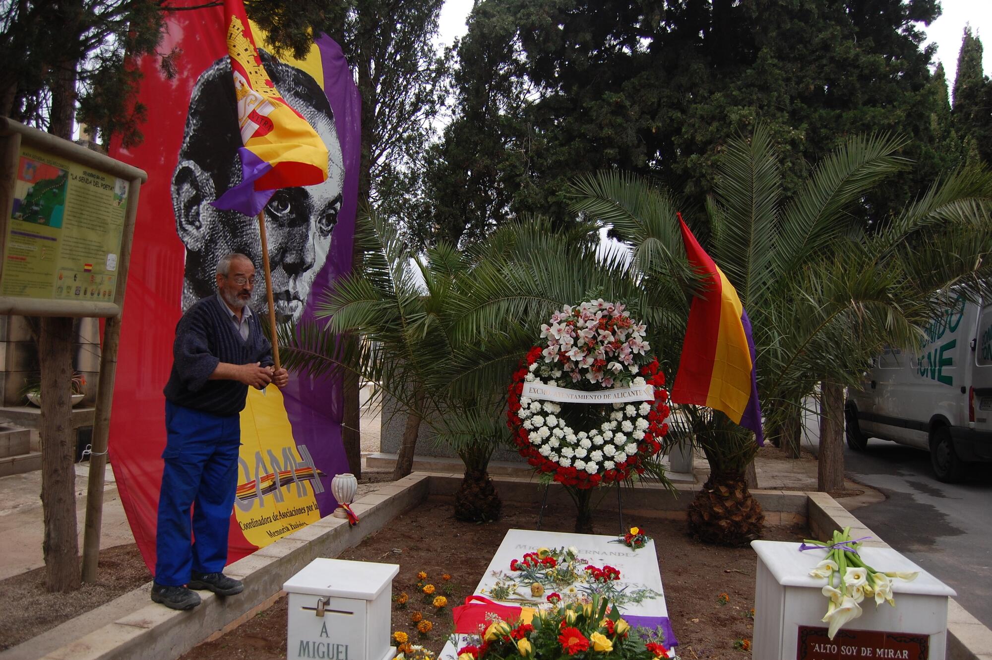 Una persona enarbola una bandera republicana ante la tumba de Miguel Hernández, en el fin de la Senda del Poeta