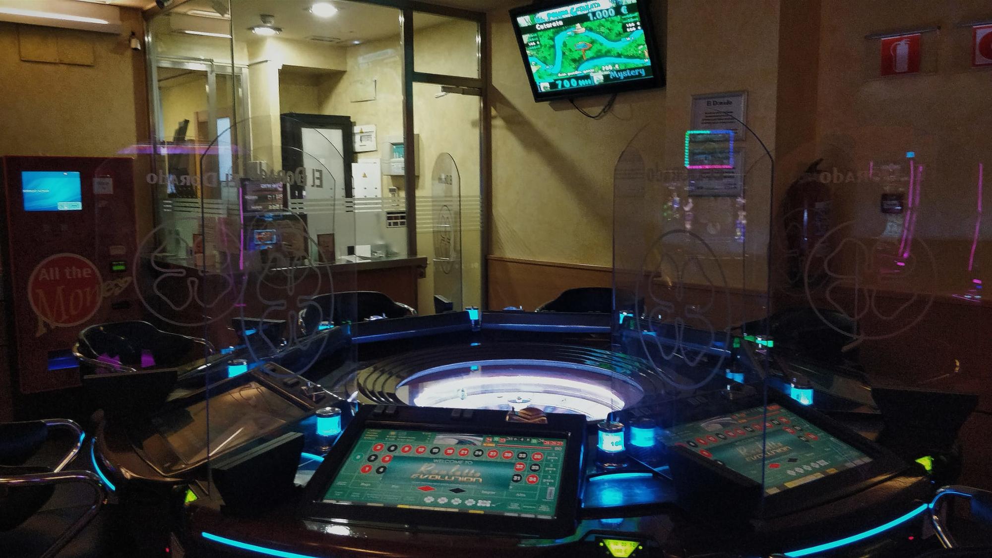 Interior del salón con la ruleta, el habitáculo de los trabajadores, la máquina de cambio y la televisión en la pared. 